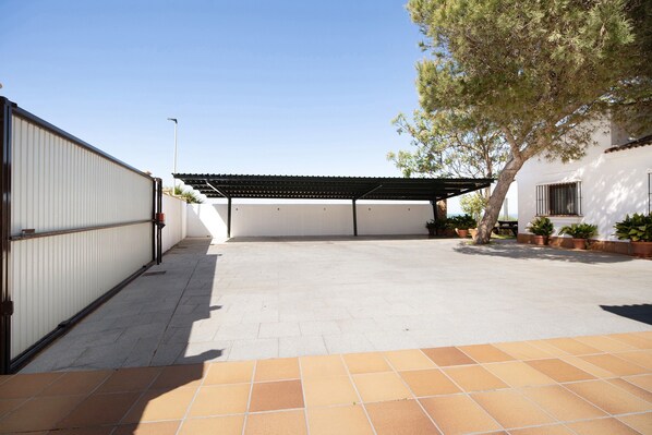 Un espacio exterior techado con piso de baldosas, una pérgola y plantas en macetas.
