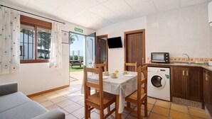 A room with a table, chairs, a washing machine, a TV, and a view of the outside.