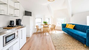 A bright kitchen with modern appliances, a dining area with a round table and chairs, and a blue sofa with a yellow pillow.