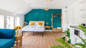 A modern bedroom with a teal accent wall, a wooden bed frame, a blue sofa, and a small bedside table with a lamp.