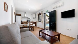 Habitación de hotel con sofá, una mesa de madera, televisión, zona de cocina y una puerta con la leyenda 'SALIDA'.