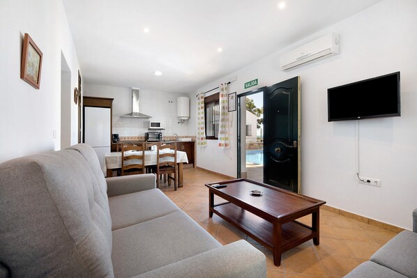 Une chambre d’hôtel avec un canapé, une table en bois, une télévision, un coin cuisine et une porte portant l’inscription « SORTIE ».