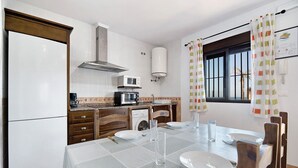 Una cocina con microondas, tostadora y lavamanos, una mesa de comedor para cuatro personas y una ventana con cortinas.