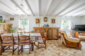 Ein Essbereich mit Holztisch und -stühlen, einer Holzkommode, einem Fernseher und Bildern an den Wänden.