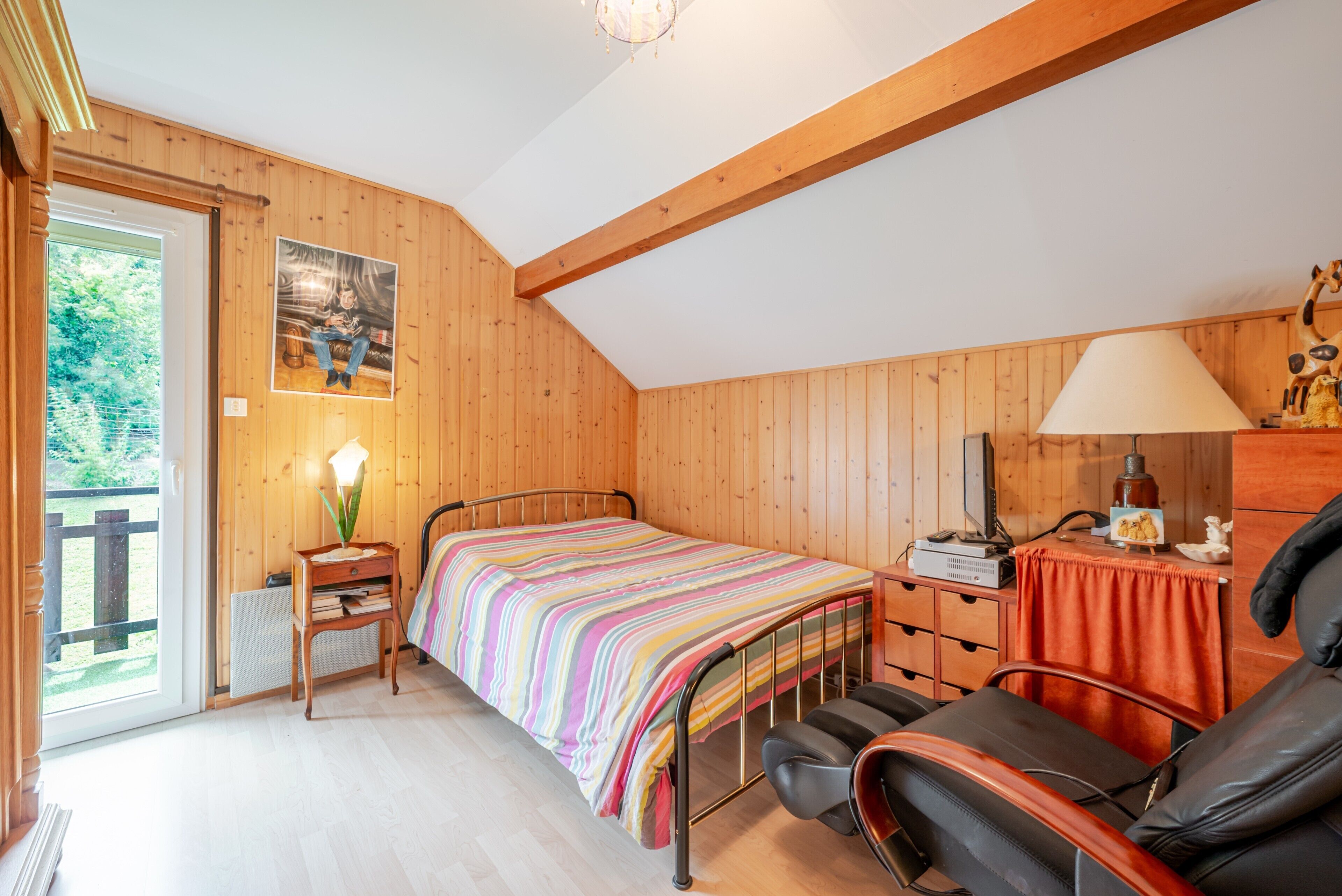 Un dormitorio con cama, una silla, un escritorio, una lámpara y una ventana.