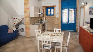Una cocina compacta con lavadora, una mesa de comedor con sillas, una puerta azul y un pequeño sofá.