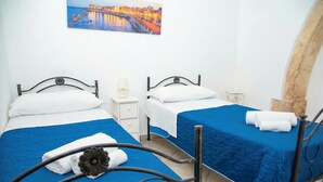 Habitación de hotel con dos camas, una mesita de noche con lámpara, un cuadro en la pared y un arco de piedra.