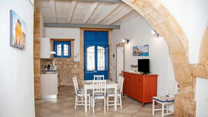 Un comedor con una mesa y sillas, una puerta azul, un muro de piedra, un televisor y un armario.