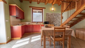 A kitchen with wooden cabinets, a dining table with chairs, a stone wall, and a wooden staircase. - Chalet 'Civico 2' with Mountain View, Balcony and Wi-Fi (Marmora)