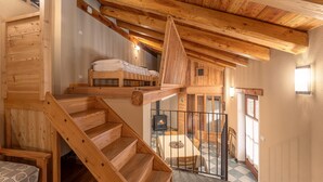Una escalera de madera lleva a un dormitorio en entrepiso con una cama y una chimenea.