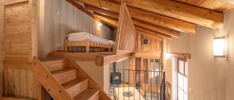 A wooden staircase leading to a loft bedroom with a bed and a fireplace.