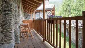Una terraza de madera con muros de piedra, una silla de madera y vistas a un paisaje montañoso.