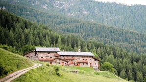 Un chalet de montagne rustique, doté d’une façade en pierre, de balcons en bois et d’un chemin de terre menant à l’entrée.