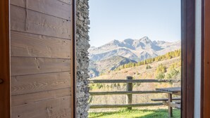 Une porte en bois donnant sur un mur de pierre, un banc en bois et une vue sur les montagnes.