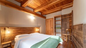 A bedroom with a wooden headboard, a bed with white linens, a green throw blanket, a wooden chair, and a built-in wooden wardrobe. - Chalet 'Civico 11' with Mountain View, Balcony and Wi-Fi (Marmora)