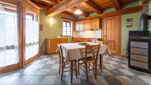 A wooden kitchen with a checkered floor, a dining table with chairs, wooden cabinets, and a wood-burning stove. - Chalet 'Civico 11' with Mountain View, Balcony and Wi-Fi (Marmora)