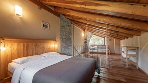Un dormitorio con techo de madera, pared de piedra, cama con ropa de cama blanca y vistas al exterior.