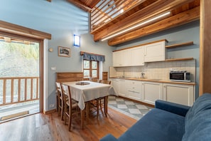 A dining area with a table and chairs, a kitchen with cabinets and a microwave, and a blue couch. - Chalet 'Civico 8' with Mountain Views, Shared Garden and Wi-Fi (Marmora)