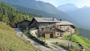 A stone house with a balcony, surrounded by a forested hillside and mountains in the background. - Chalet 'Civico 7' with Mountain View, Shared Terrace and Wi-Fi (Marmora)