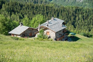 A stone house with a sloped roof, surrounded by a forested hillside.