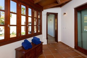 A room with large wooden-framed windows, a wooden bench with towels, and a tiled floor.
