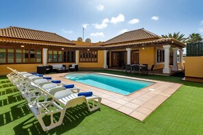 A pool area with lounge chairs, a pool, and a patio with outdoor furniture.