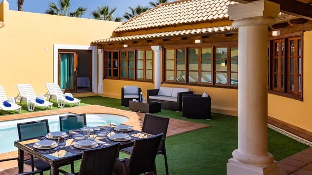 Un espace aménagé au bord de la piscine, avec une table à manger pour quatre personnes, des chaises longues et un coin salon couvert offrant une vue sur la piscine.