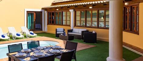 A poolside area with a dining table set for four, lounge chairs, and a covered seating area with a view of the pool.