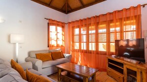Un salon avec un canapé, une table basse, un téléviseur posé sur un meuble en bois et des rideaux orange.