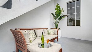 A wooden sofa with cushions, a glass table with a bottle and glass, and a potted plant.