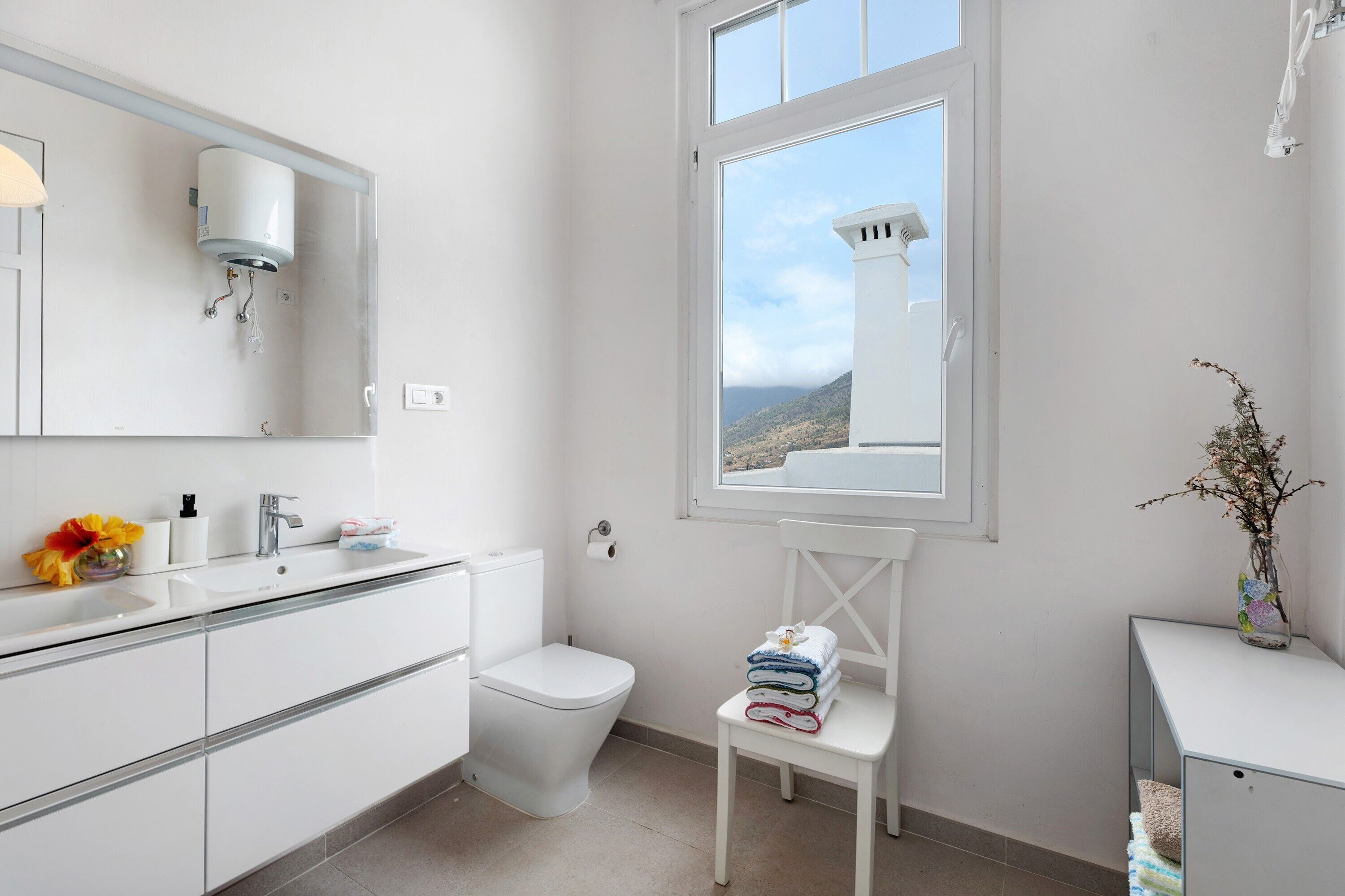 A modern bathroom with a toilet, sink, mirror, and a window with a view of a mountainous landscape.