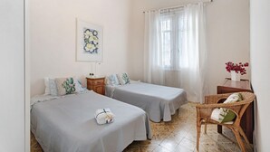 A bedroom with two beds, a nightstand, a chair, a window with curtains, and a painting on the wall.