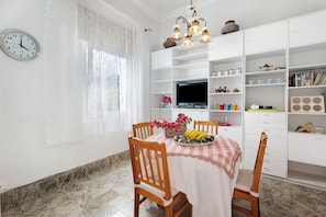 Un coin repas avec une table dressée pour deux personnes, un téléviseur posé sur un meuble et un buffet blanc avec des étagères.