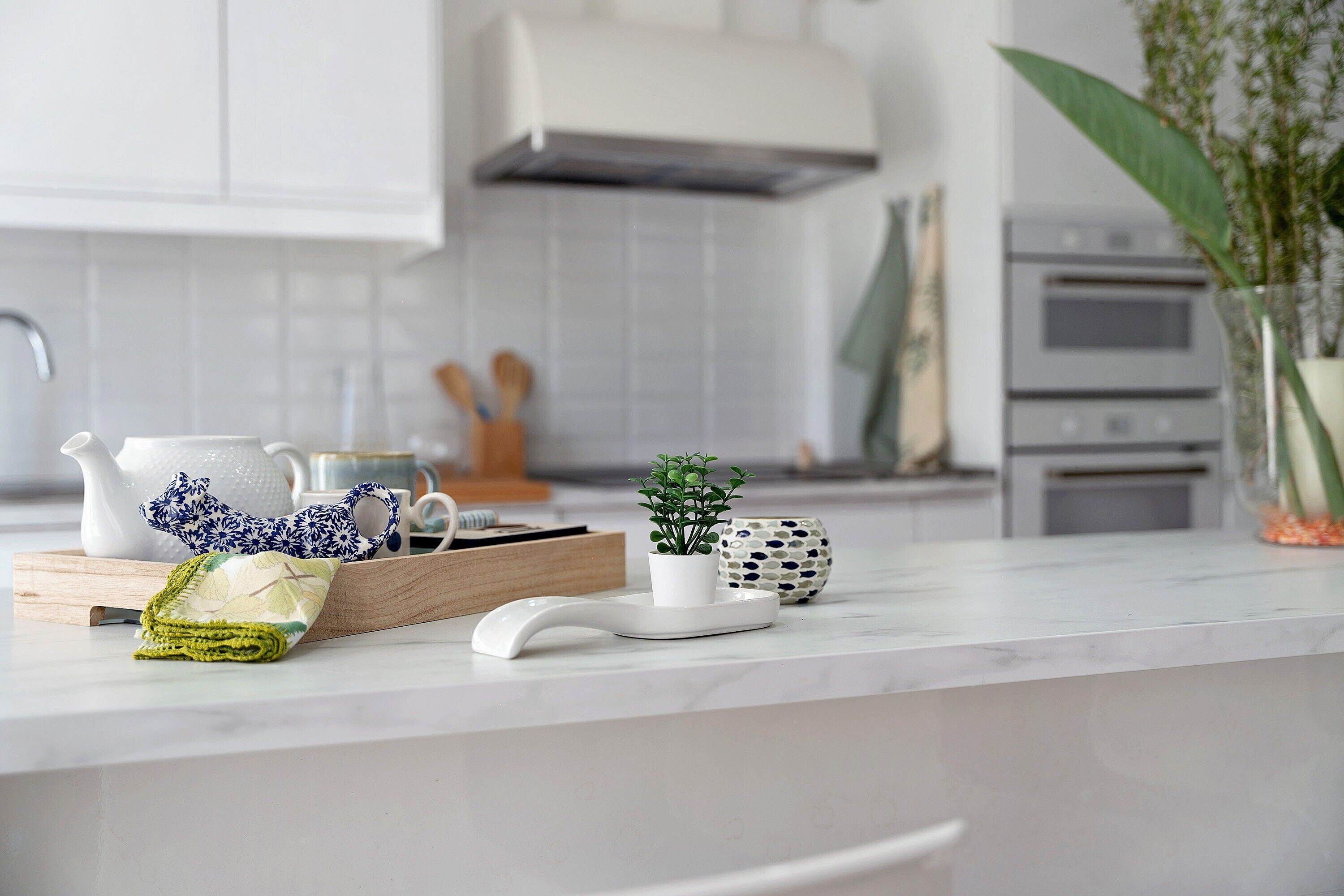 Un comptoir de cuisine avec une théière blanche, une tasse bleue et blanche à motifs, une petite plante en pot, un sac en tissu tissé et une tasse en céramique.