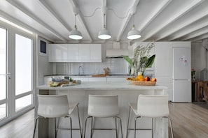 Eine moderne Küche mit weißen Schränken, einer zentralen Kochinsel mit Barhocker, Pendelleuchten und einem Kühlschrank.