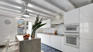 A modern kitchen with white cabinets, a marble island, stainless steel appliances, and a large window.