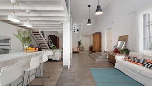 A spacious living area with a kitchen, white furniture, and a staircase leading to another level.