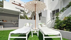 Two white lounge chairs with pillows, a table with a cup and tray, and a beige umbrella.