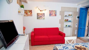 Een woonkamer met een rode bank, een televisie op een witte kast, een tafel met patroon en een blauwe deur.
