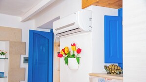 Een kamer met een blauwe deur, een witte airconditioning, een bloevas met rode en gele tulpen aan de muur, en een klein schildpadbeeldje op een betegelde toonbank.