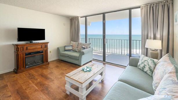 Een woonkamer met een flatscreen televisie, een bank, een salontafel en een balkon met uitzicht op zee.