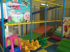 Un espace de jeux intérieur équipé d’un filet de sécurité, d’un sol rembourré et de structures de jeu colorées.