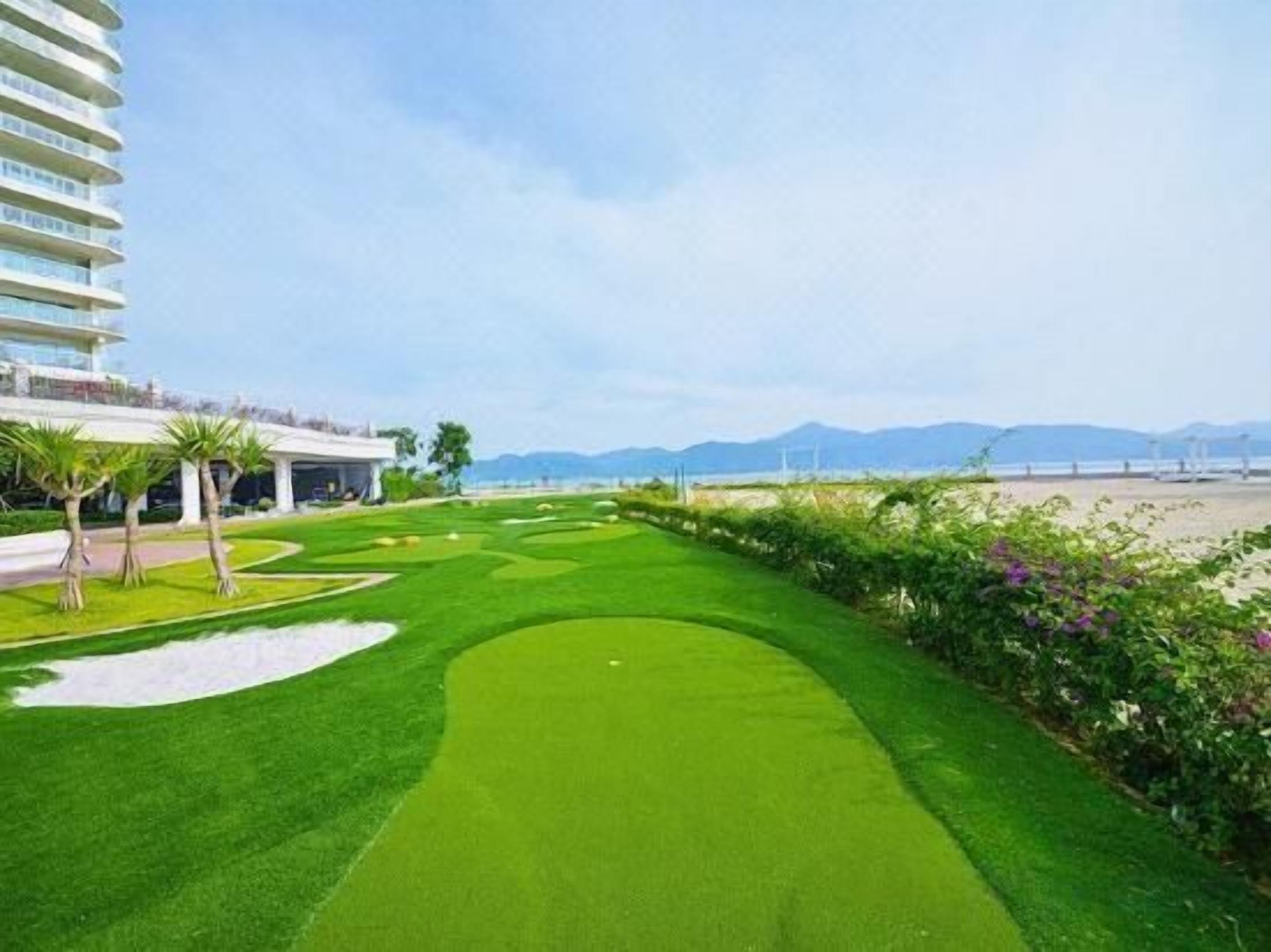 Un campo de golf con un edificio a la izquierda y una playa al fondo.