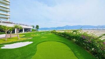 Un campo de golf con un edificio a la izquierda y una playa al fondo.