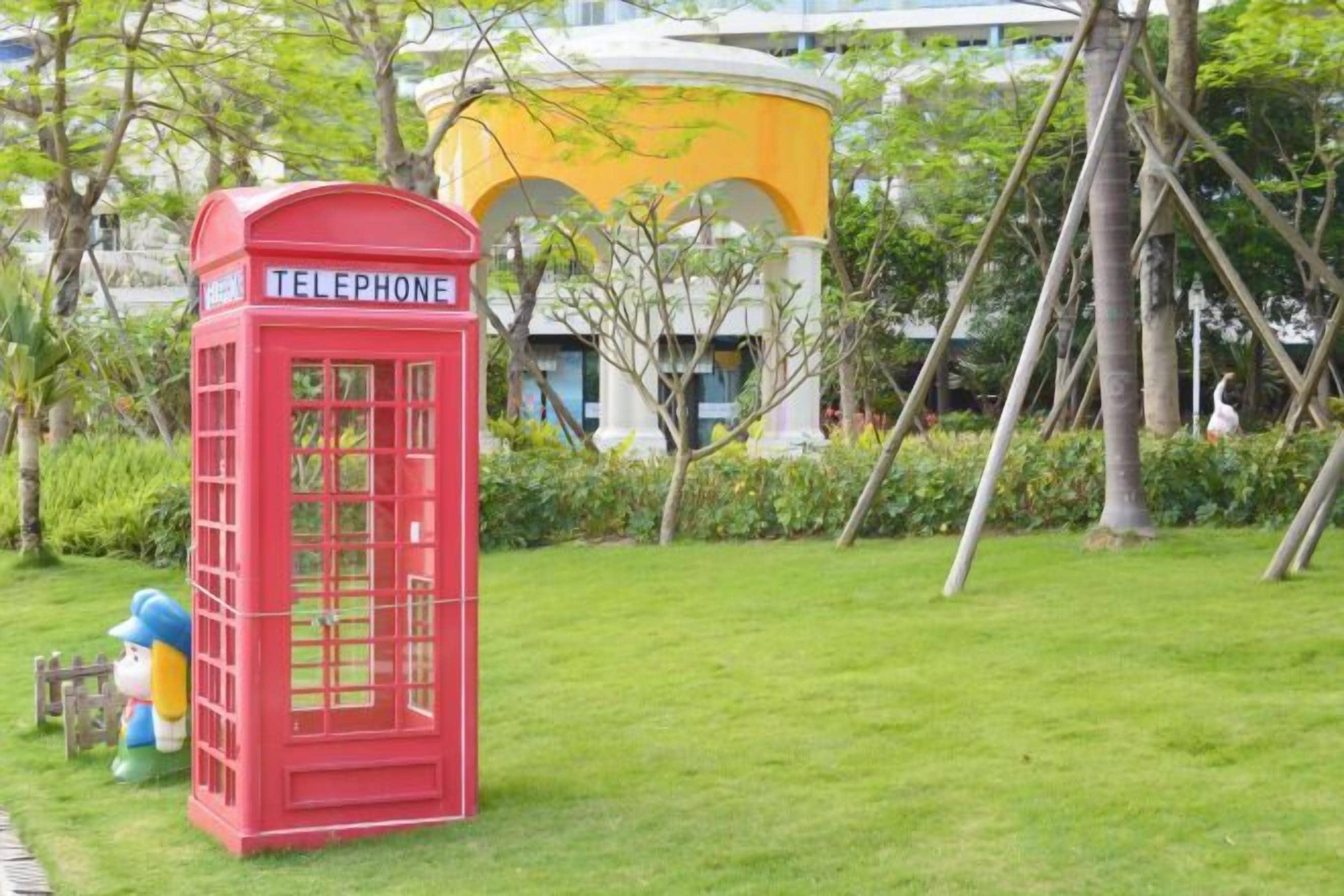 A red telephone booth in a grassy area with a building in the background.