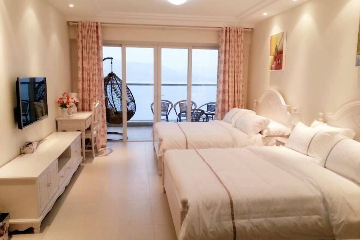 Habitació d'hotel amb dos llits, televisió, escriptori i balcó amb cadires.