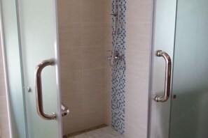 Un espace douche doté de portes en verre, d’un mur carrelé et d’un pommeau de douche.