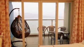 A balcony with a bed, chairs, and a hanging chair overlooking a body of water.