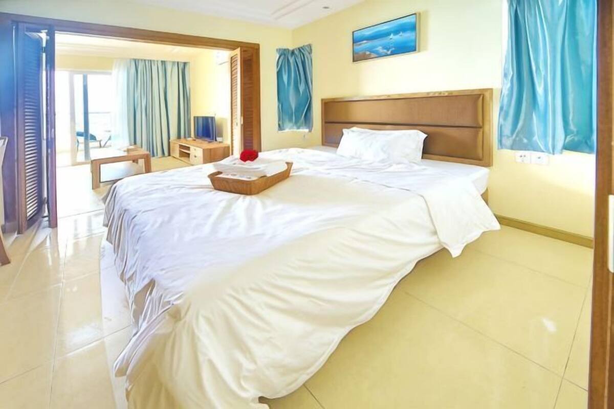 Habitació d'hotel amb un llit gran, un panell de fusta al capçal, una taula amb cadira i una finestra amb cortines.