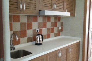Une cuisine avec des meubles en bois, un plan de travail blanc, une bouilloire en acier inoxydable et un dosseret carrelé.